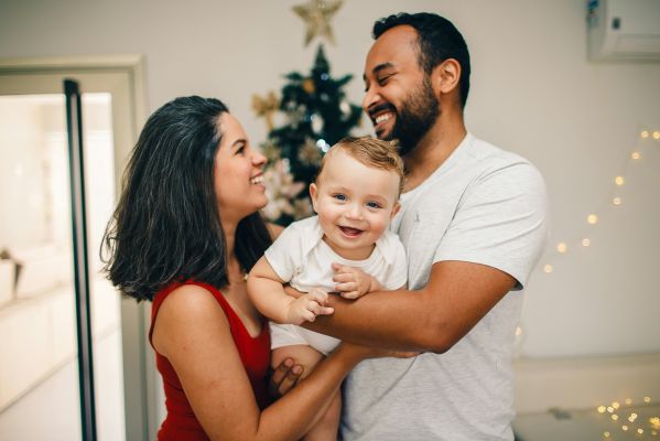 A man and woman holding a baby in front of a christmas tree
