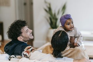 Unrecognizable ethnic mom interacting with cute toddler child near content bearded father in house room